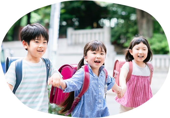 3人の小学生が手を繋いて楽しそうに歩いている
